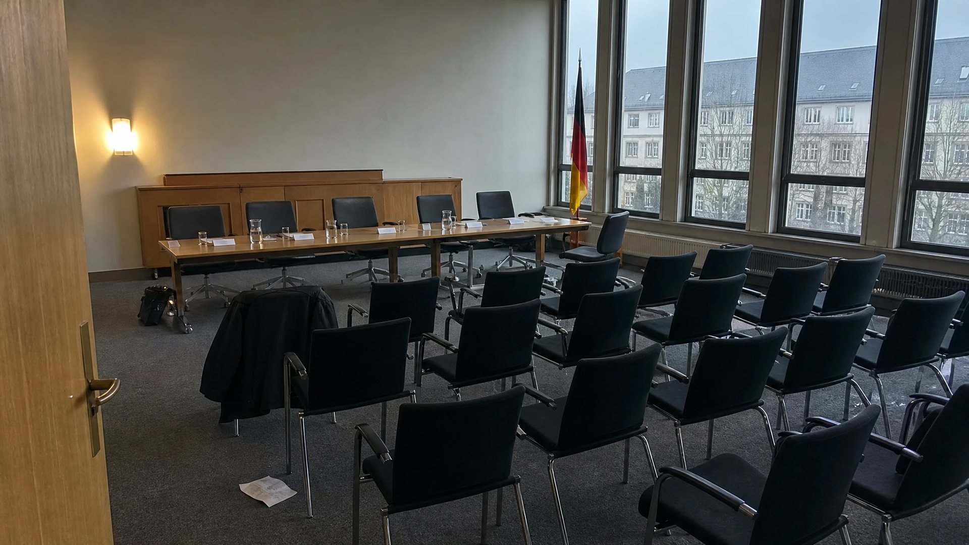 Leerer Anhörungssaal nach einer Konsultation: umgedrehte Namensschilder, halbvolle Wassergläser, Stellungnahmen mit der Schrift nach unten