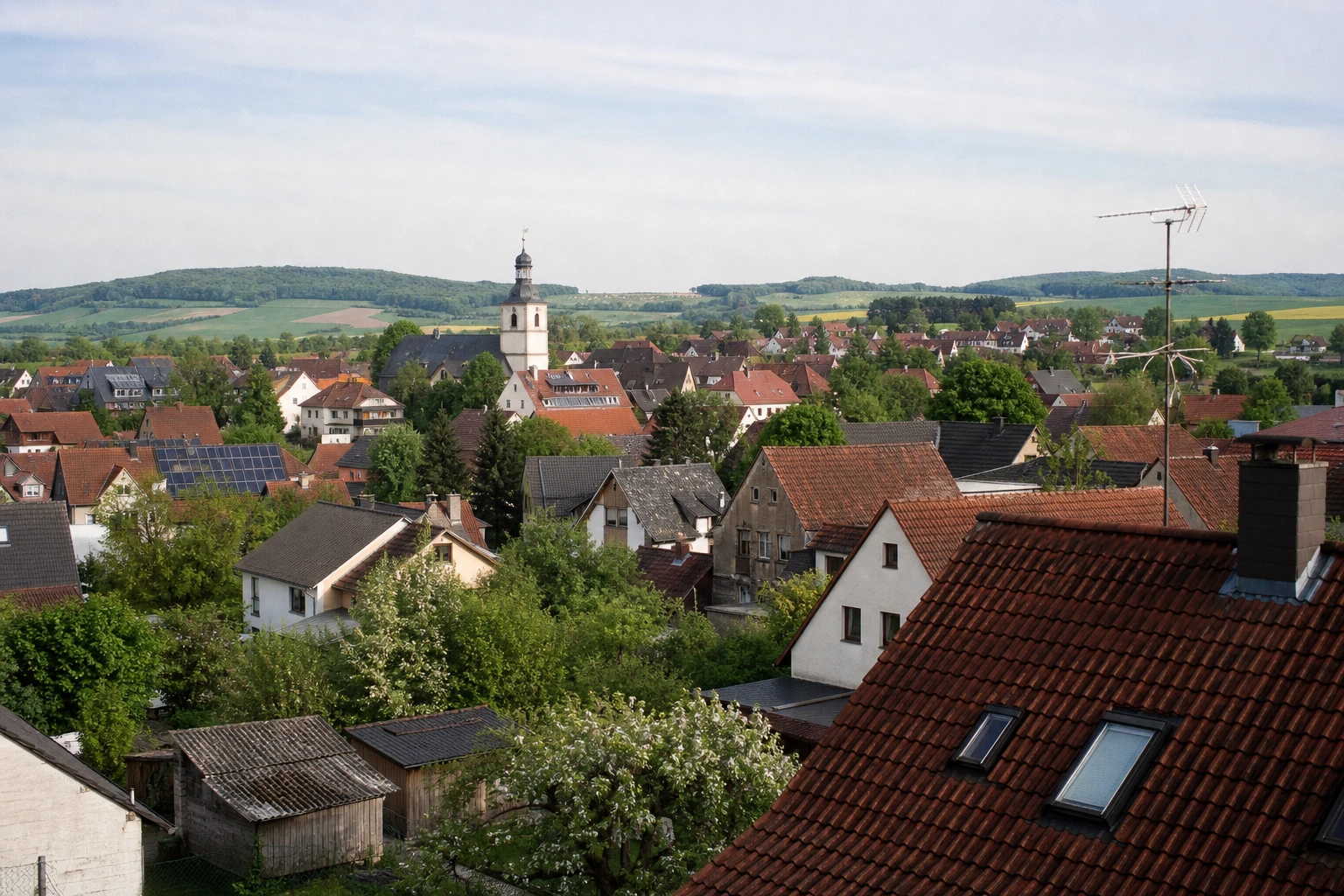 Blick über eine deutsche Kleinstadt mit Kirchturm, roten Ziegeldächern, vereinzelten Solardächern und Feldern am Horizont