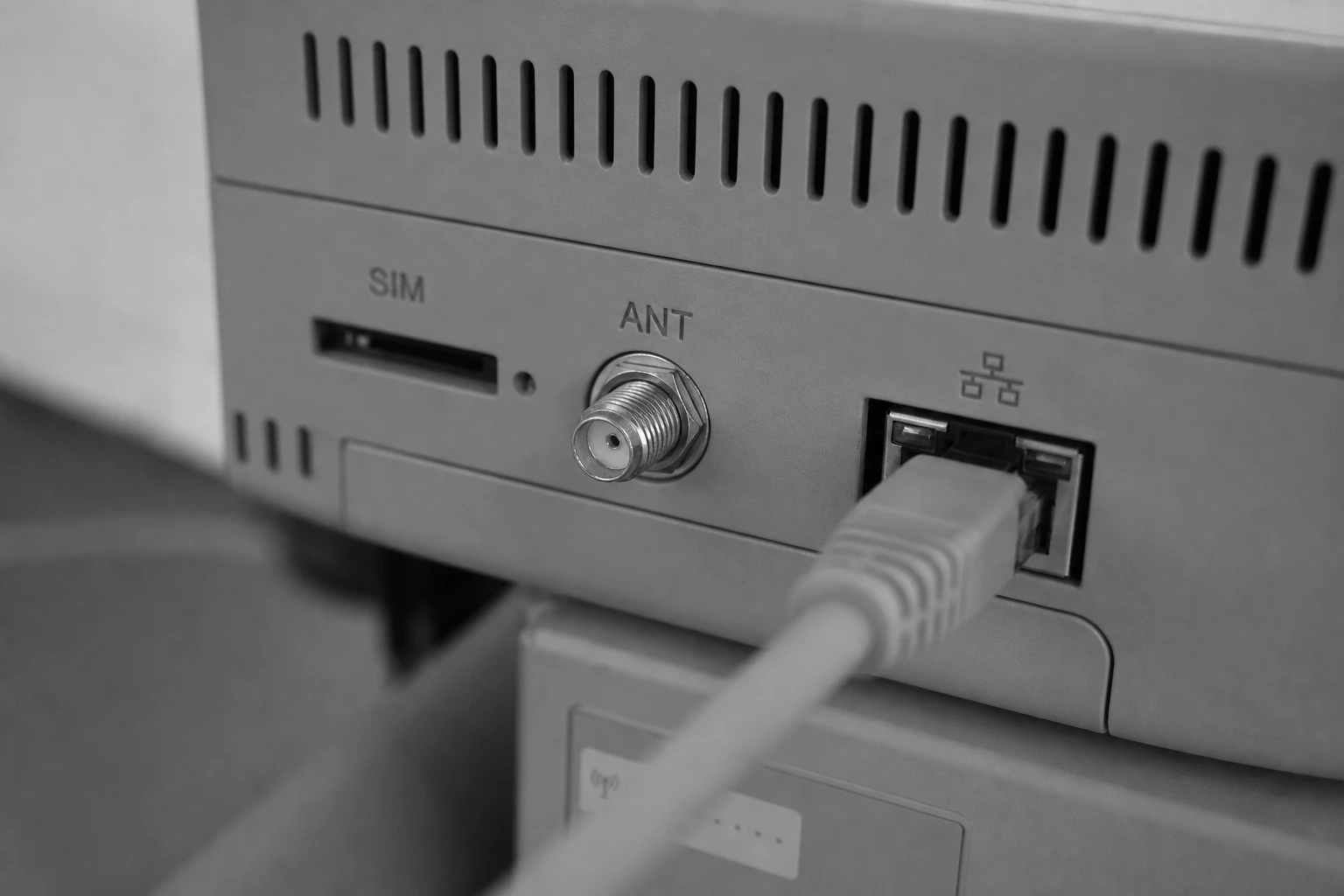 Detailaufnahme eines Smart-Meter-Gateways mit SIM-Steckplatz, Antennenanschluss und Ethernet-Port, Schwarzweiss