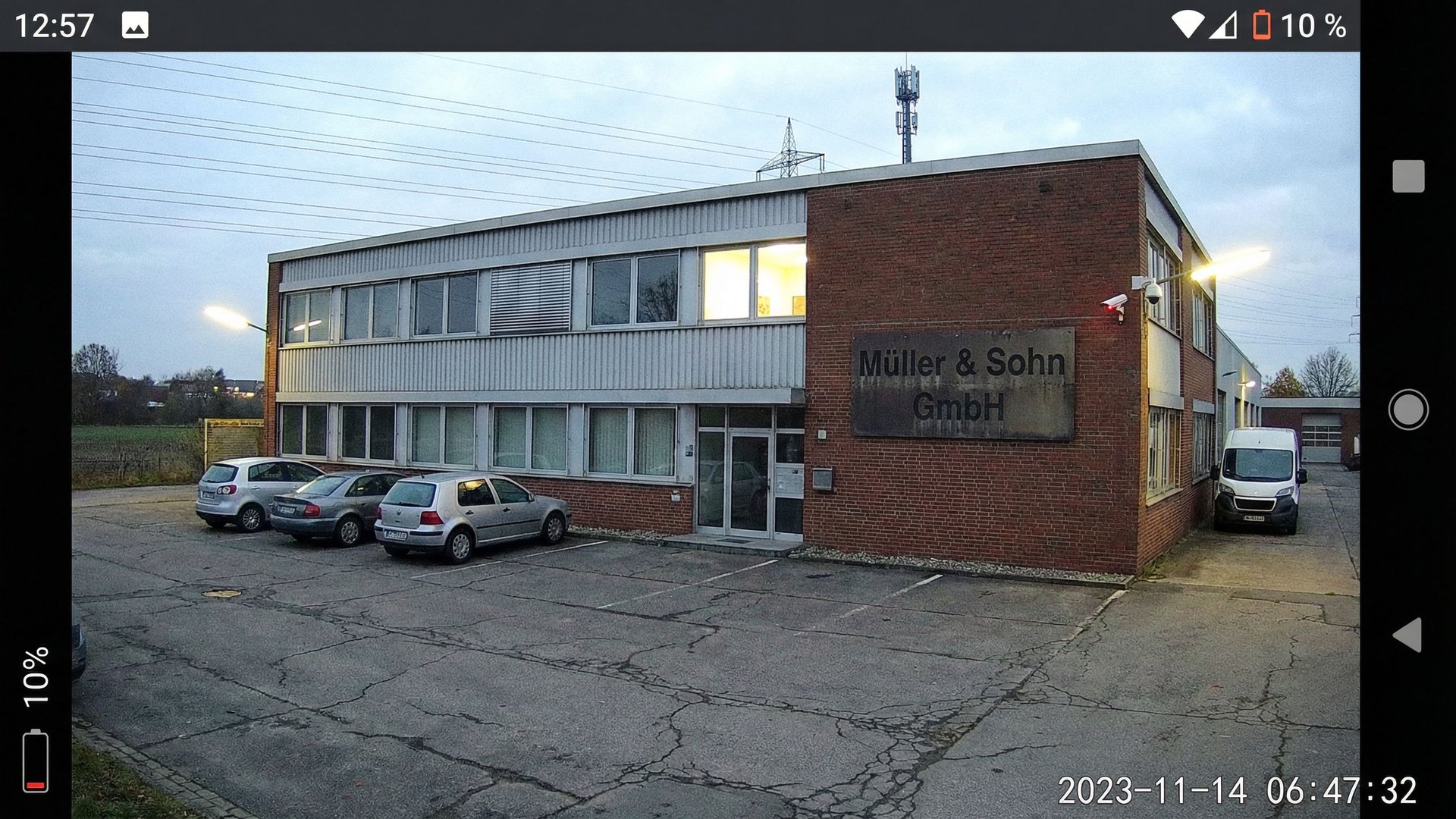 Industriegebäude am Stadtrand mit Hochspannungsleitungen und Überwachungskamera, symbolisch für ungeschützte digitale Infrastruktur