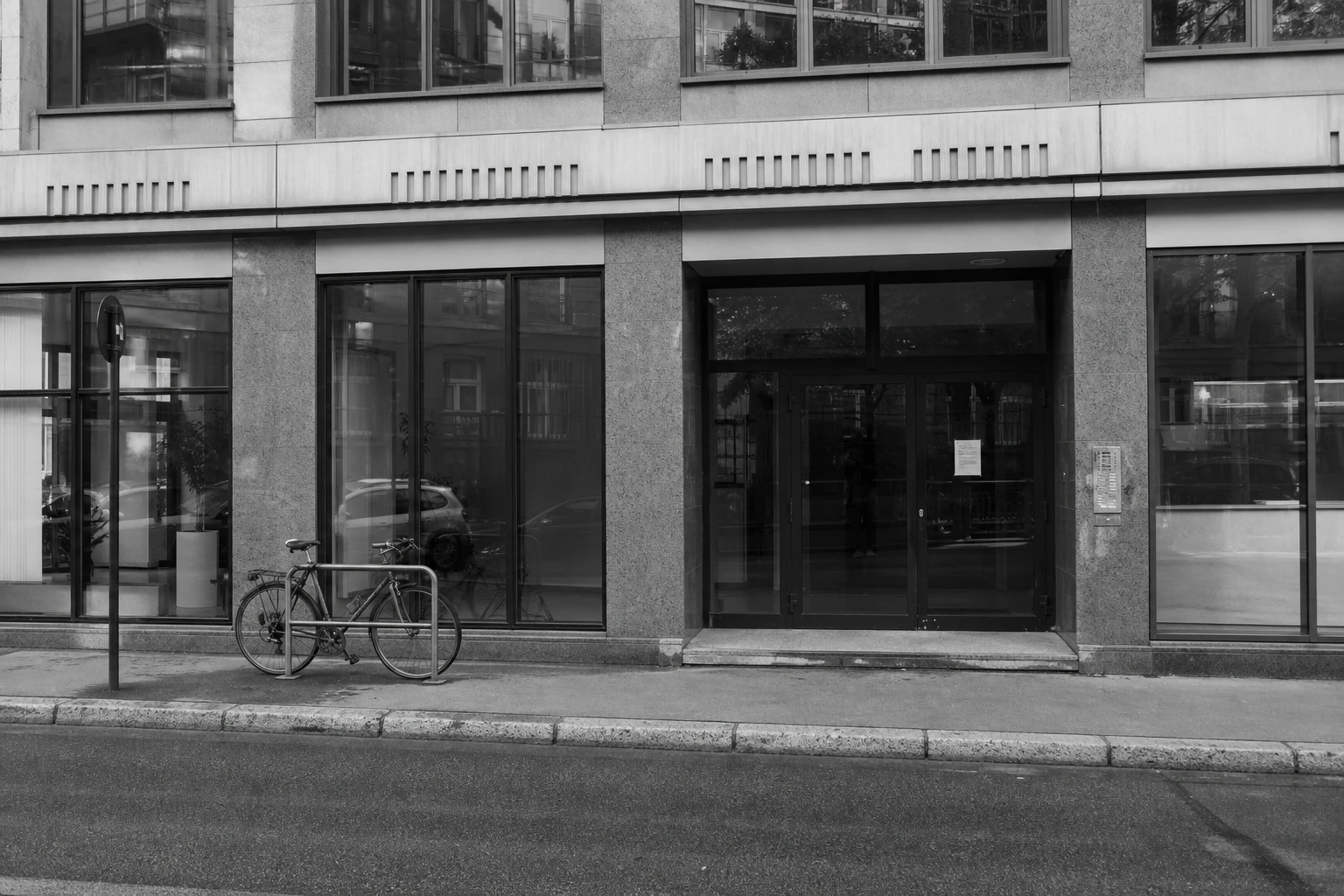Glaseingang und Fassade eines schlichten städtischen Bürogebäudes mit angeschlossenem Fahrrad