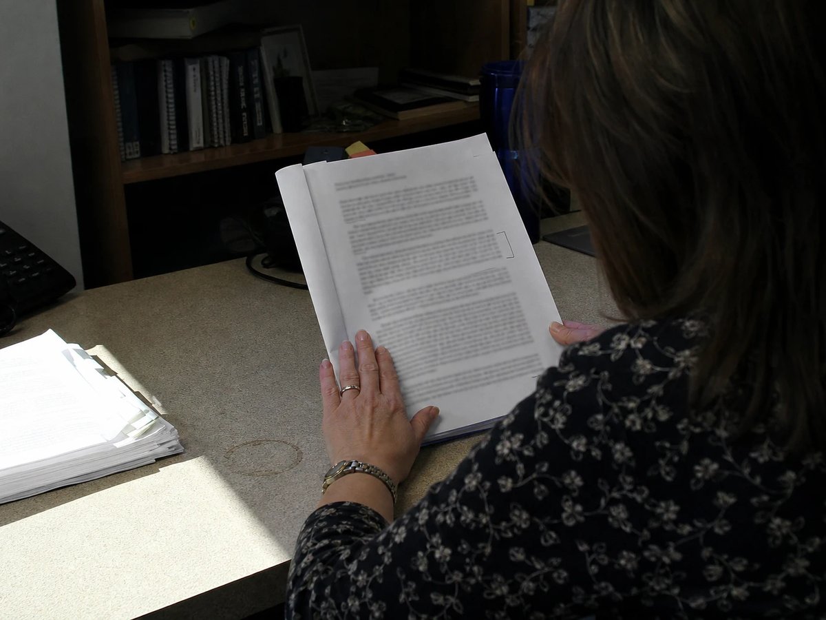 Over the shoulder of a regulatory manager at her desk working through a thick stapled draft ruling document