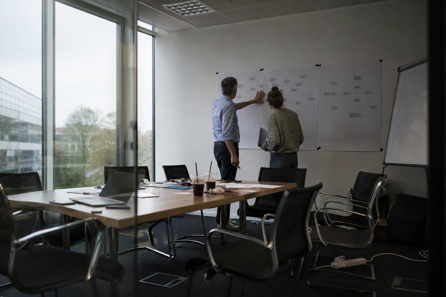 Architecture workshop at a utility: two colleagues in front of a wall-wide plotter print of the system landscape