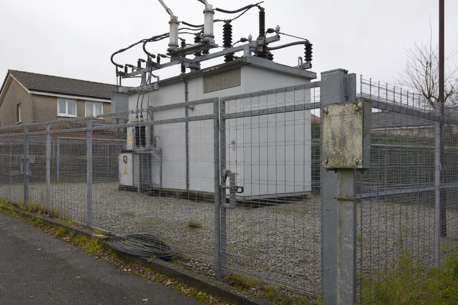A compact local distribution substation behind a fence on a residential street