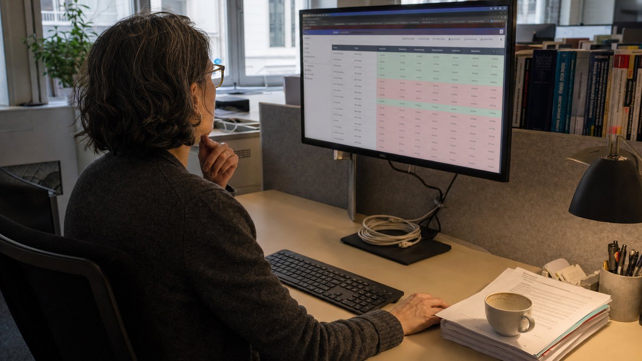 Senior software architect reviewing AI model benchmark comparison results on a wall-mounted monitor in a Frankfurt dev office