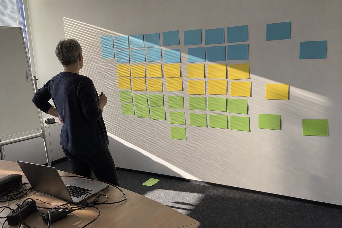 Enterprise architect in front of a wall of coloured cards arranged as a capability map, afternoon light through the blinds